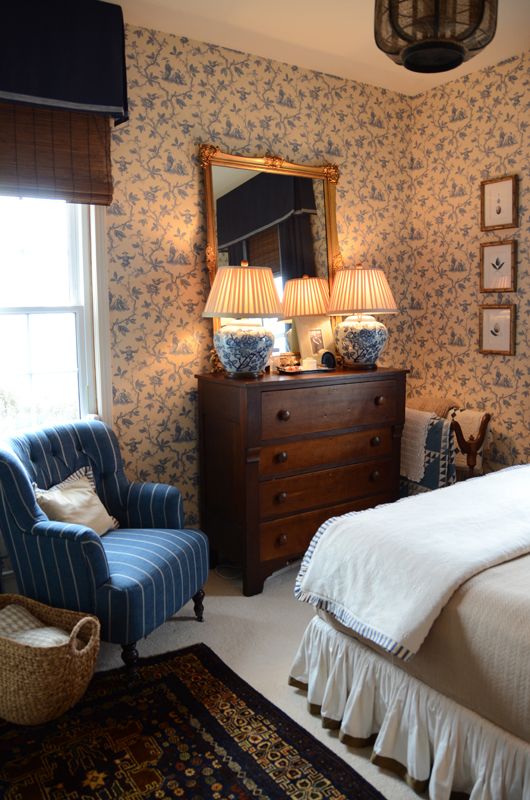 a bed room with a neatly made bed next to a dresser and a chair in front of a window