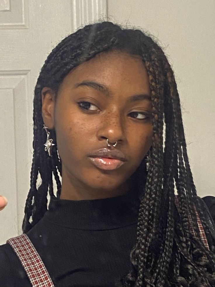 a woman with braids and piercing on her nose pointing at the camera while wearing a black shirt