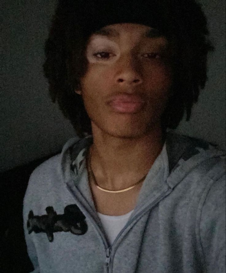 a young man with dreadlocks wearing a gray sweatshirt and black hat is taking a selfie