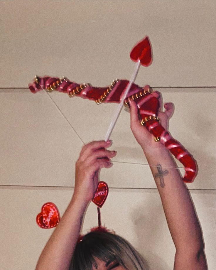 a woman holding up two candy hearts on top of her head with one heart attached to the string