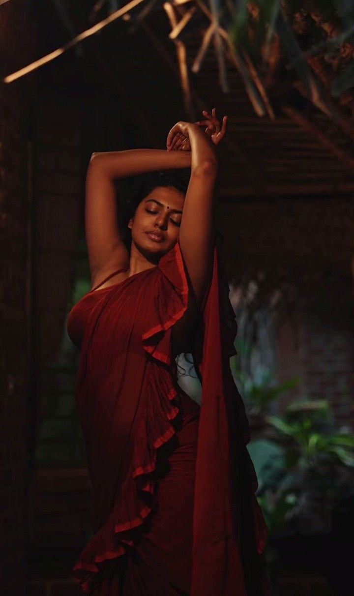 a woman in a red dress holding her hands behind her head and posing for the camera