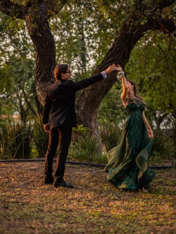 a man and woman are dancing in the grass under some trees at sunset with their arms outstretched