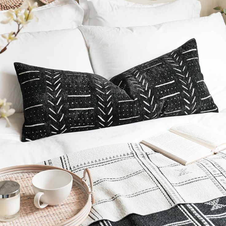 two black and white pillows sitting on top of a bed next to a tray with an open book