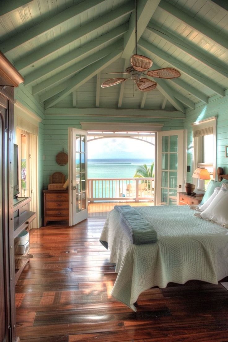 a bedroom with wood floors and a bed in the middle of the room, looking out onto the ocean