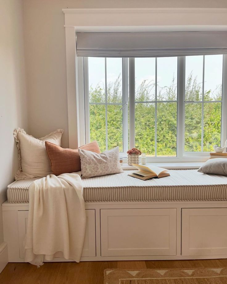 a window seat with pillows on it and a book in front of the window sill