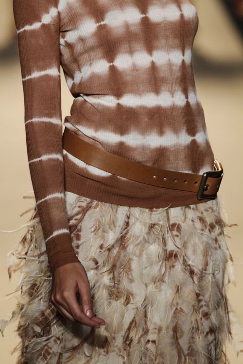 a woman wearing a brown and white sweater with feathers on the skirt, belted around her waist