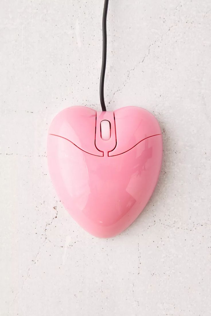 a pink heart shaped computer mouse hanging from a cord on a white wall with a black cord