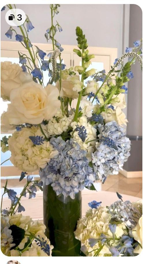 a vase filled with white and blue flowers on top of a table next to a mirror