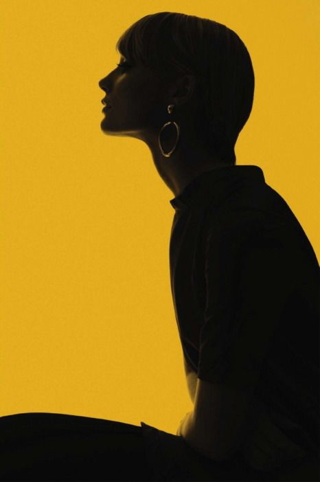 the silhouette of a woman sitting in front of a yellow wall with her head turned to the side