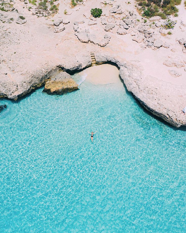 two people are swimming in the clear blue water near an arch shaped rock formation,