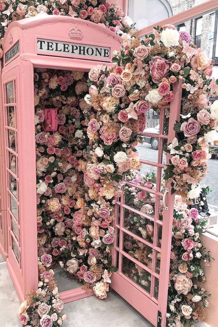 a pink phone booth covered in flowers and greenery with the words instagram on it