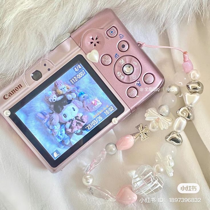 a pink cell phone sitting on top of a white blanket next to beads and charms