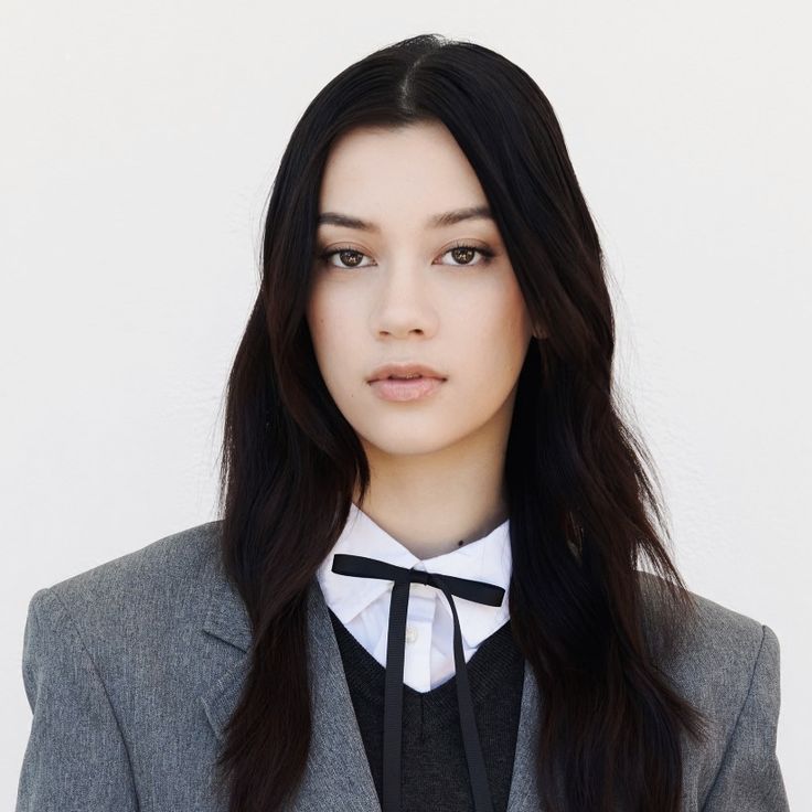 a woman with long black hair wearing a suit and bow tie