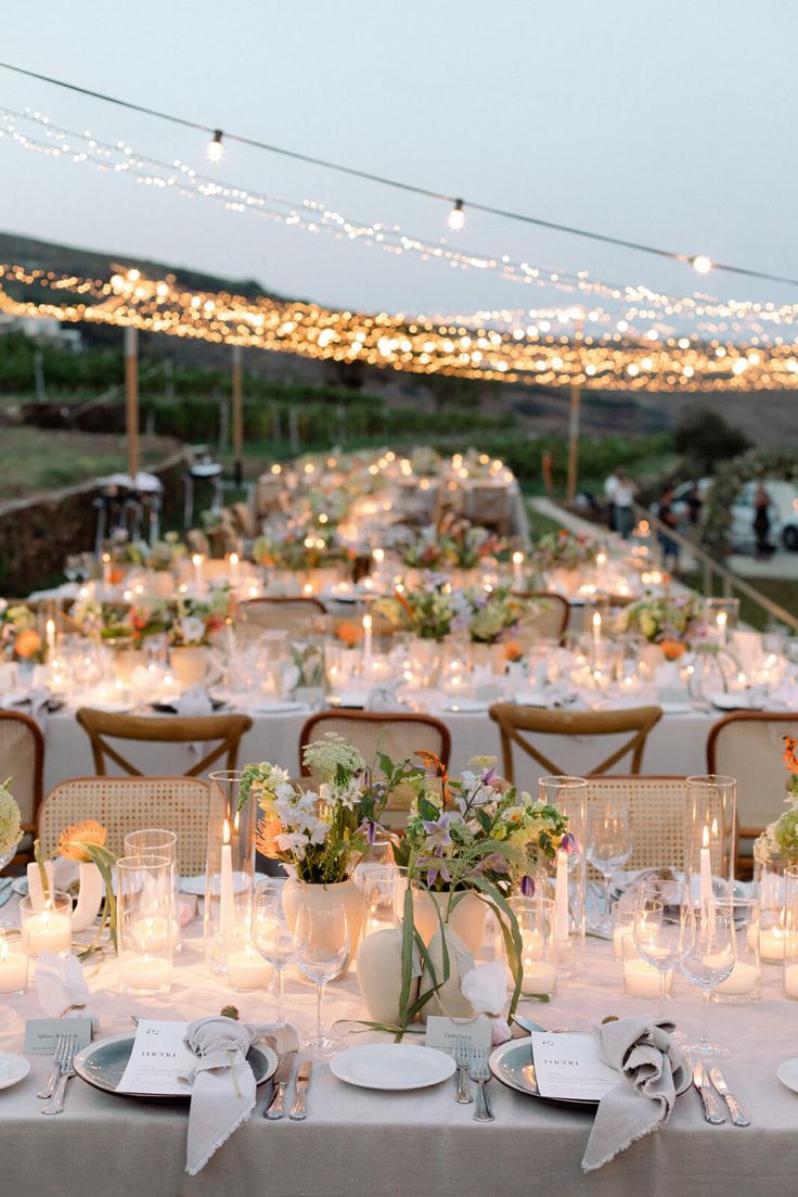 a long table is set with white plates and silverware for an outdoor wedding reception