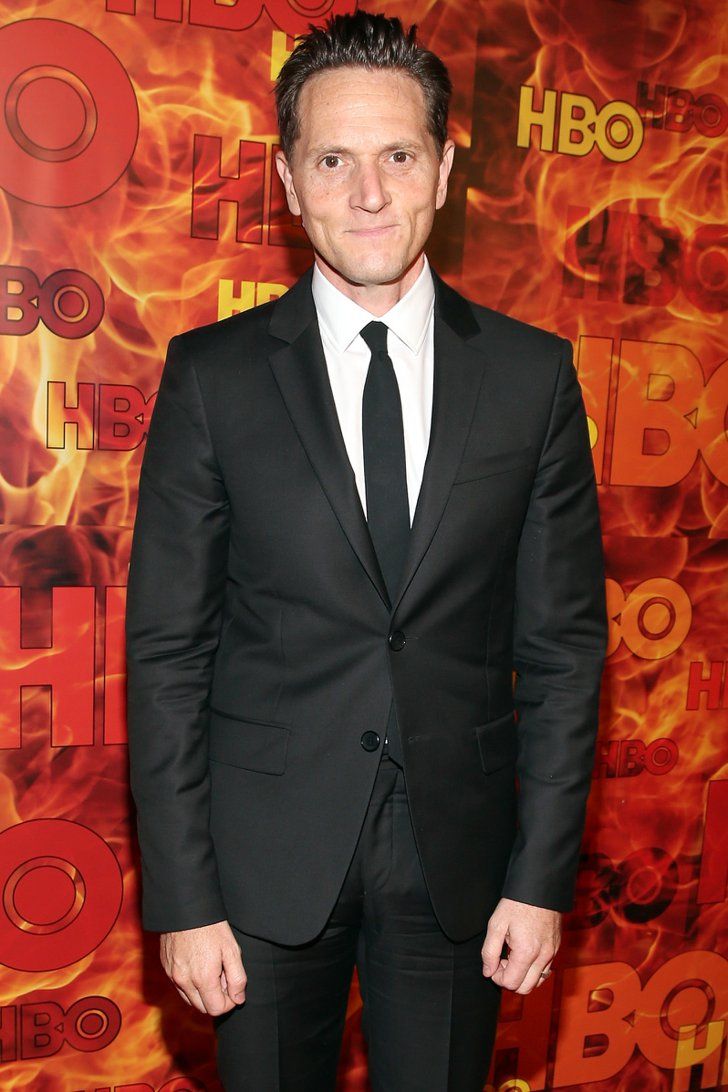 a man in a suit and tie standing on a red carpet with flames behind him