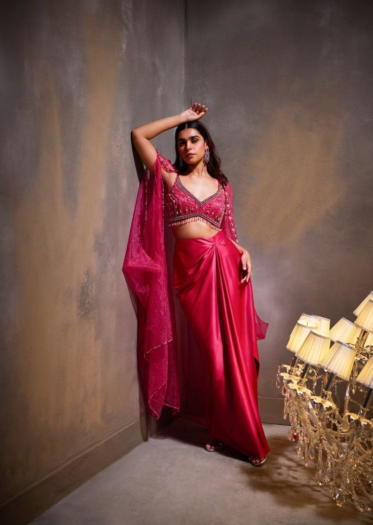 Our rose cape set presents a blend of feminine grace with its flowing skirt and hand-embellished blouse. The billowing cape adds an opulent touch to the ensemble, adorned with delicate embellishments. Elegant Draped Pink Lehenga, Elegant Pink Draped Sets, Elegant Draped Pink Sets, Festive Pink Dress With Cape Sleeves, Pink Draped Lehenga For Party, Pink Embellished Sets With Cape Sleeves, Pink Cape Sleeves Dress With Sheer Dupatta, Pink Party Sets With Cape Sleeves, Pink Georgette Dress With Cape Sleeves