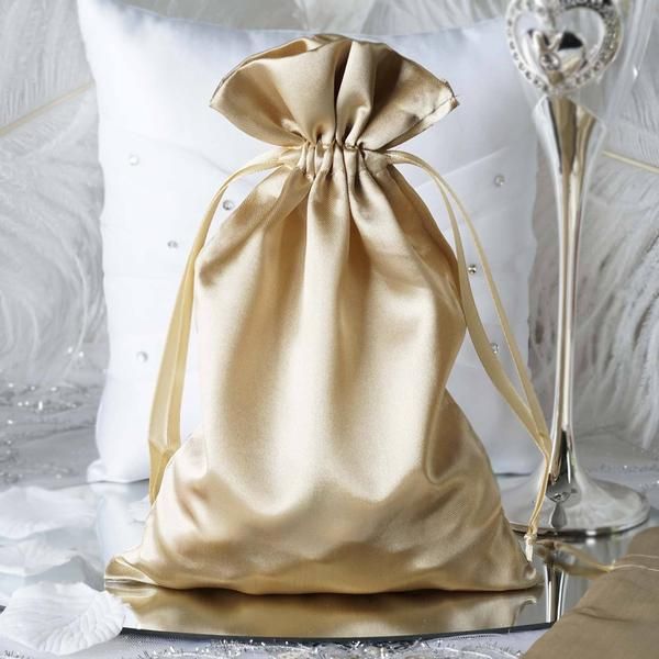 a gold satin bag sitting on top of a white pillow next to a silver vase