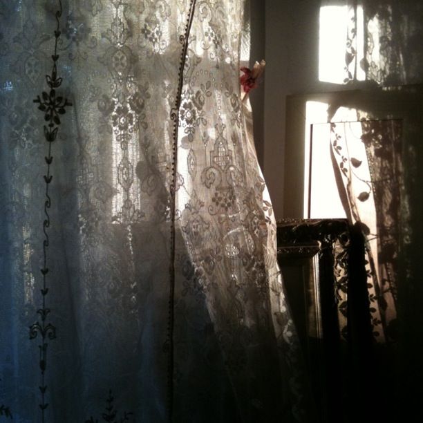 the curtain is open in front of the window with sunlight coming through it and there are flowers on the sheer curtains