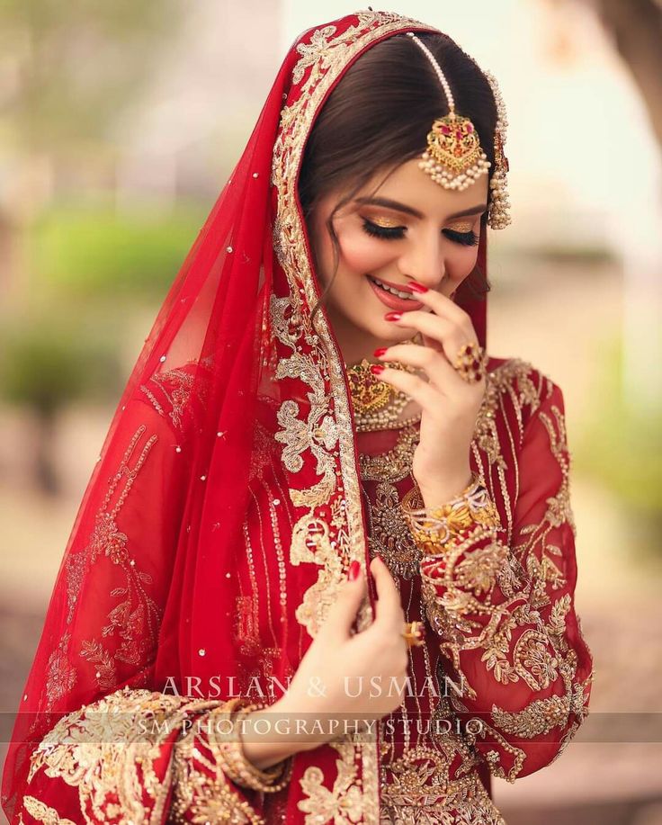 a woman in a red and gold bridal outfit with her hands to her mouth