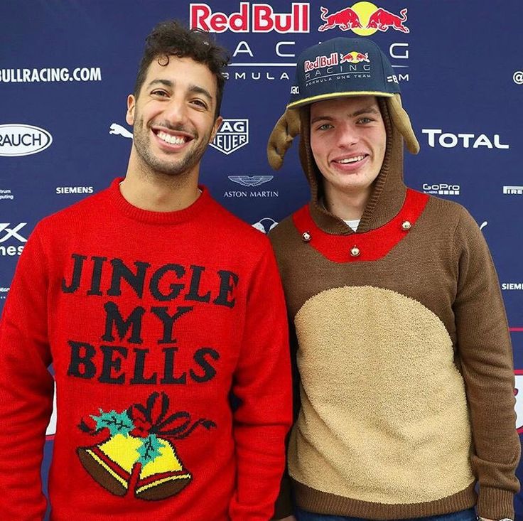 two young men standing next to each other in front of a red bull sign wearing ugly sweaters