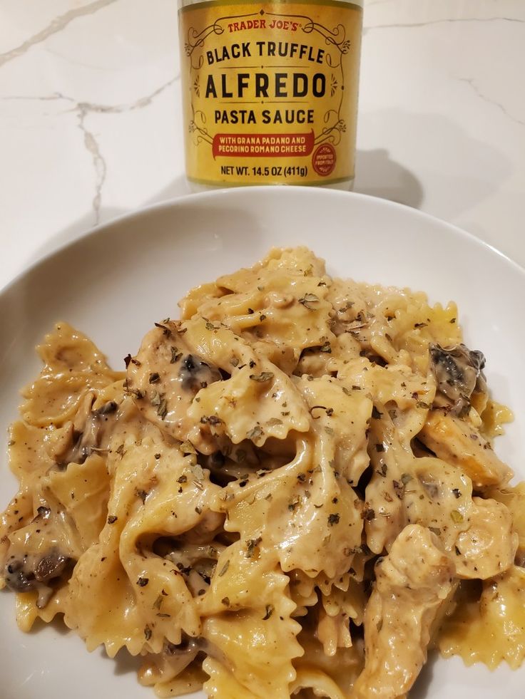 a white plate topped with pasta covered in sauce next to a jar of black truffle alfredo