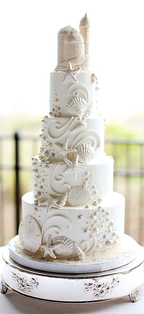 a three tiered white wedding cake with seashells on it