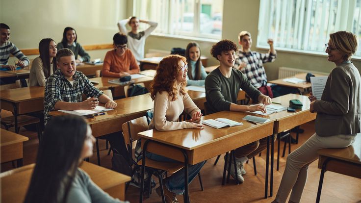 a group of people sitting at desks in a classroom with one woman standing up