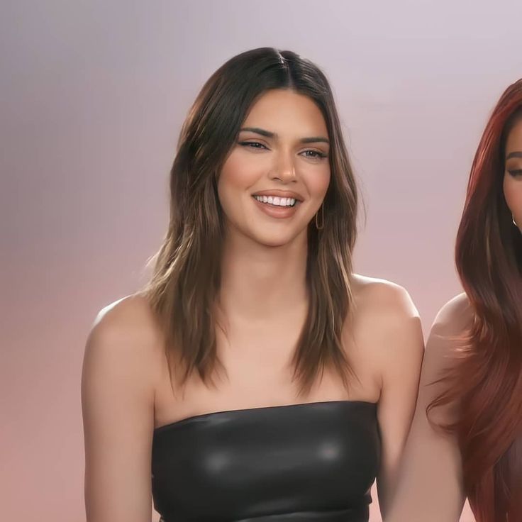 two beautiful young women standing next to each other in front of a pink background and smiling at the camera