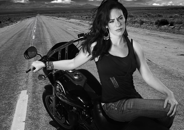 a woman is sitting on a motorcycle in the middle of an empty road with mountains in the background