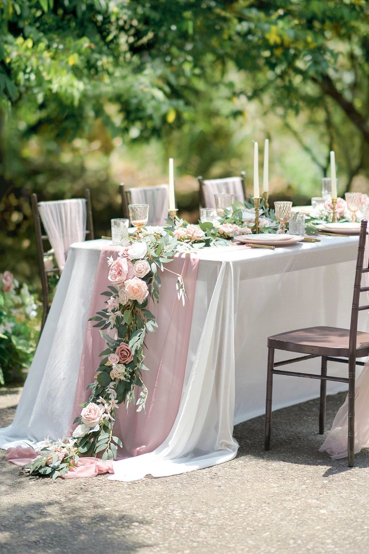 the table is set with white linens and pink flowers, greenery and candles