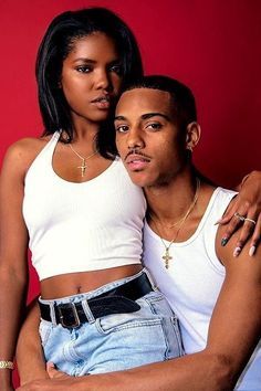 a young man and woman posing for a photo in front of a red wall with their arms around each other