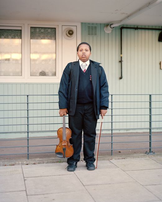 a man standing in front of a building holding a violin and wearing a black suit