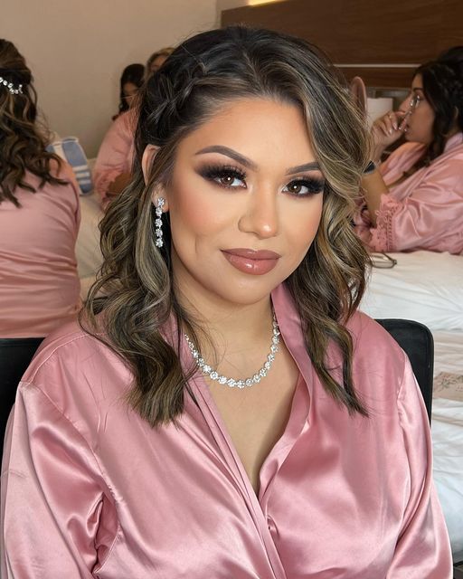 a woman sitting on top of a bed wearing a pink shirt and pearl necklaces