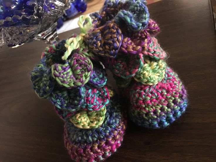 crocheted baby booties sitting on top of a table next to a glass vase