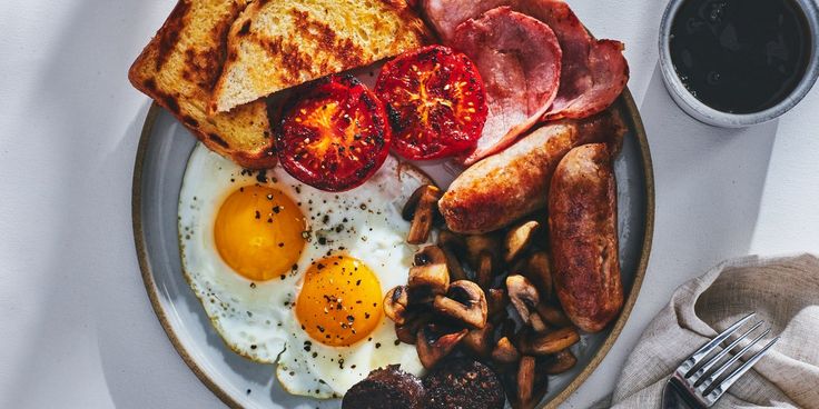 a plate with eggs, toast, mushrooms and tomatoes on it next to a cup of coffee