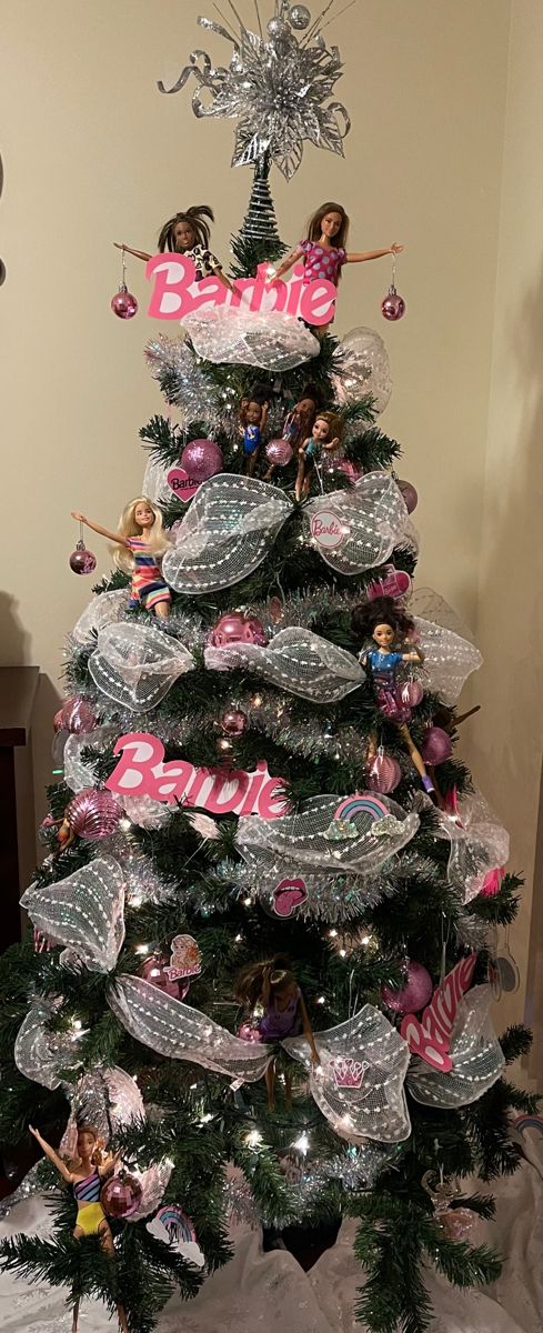 a decorated christmas tree with barbie dolls on top and pink ribbon around the base,