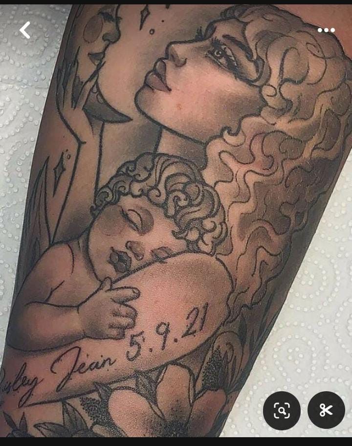 a woman holding a baby in her arms with tattoos on it's arm and chest