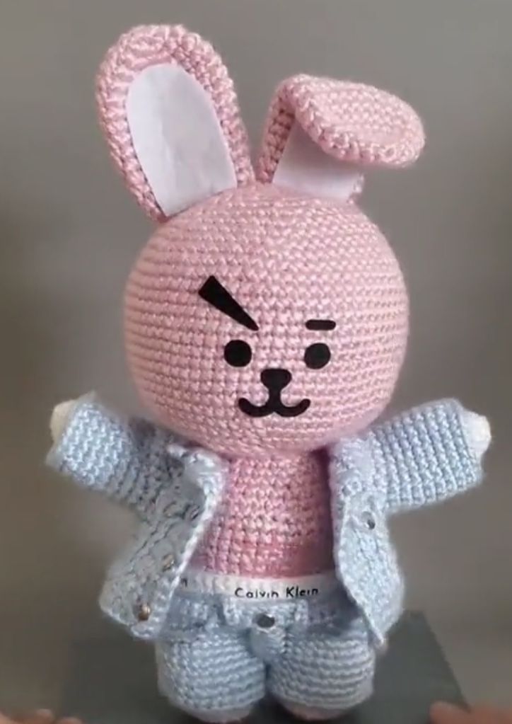 a crocheted pink bunny doll with blue pants and jacket on it's chest