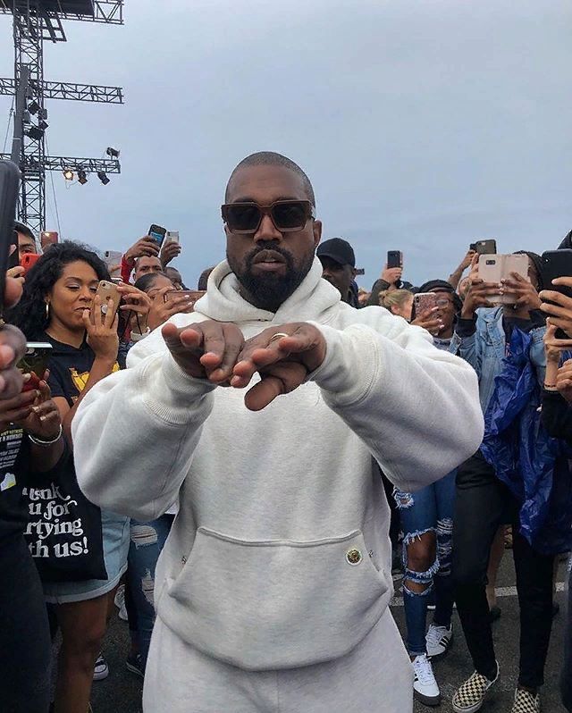 a man in a white hoodie pointing at the camera with people taking pictures behind him