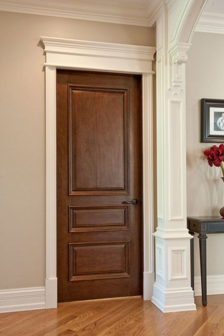 a wooden door in the middle of a room next to a vase with red flowers