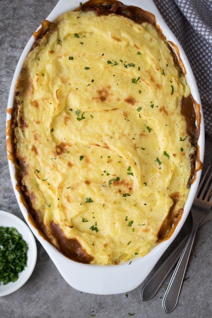 a casserole dish with meat and cheese in it next to a bowl of parsley