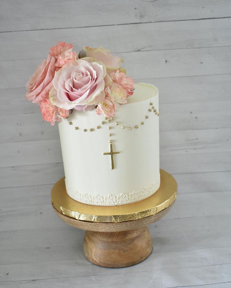 a white cake with pink flowers and a cross on the top is sitting on a stand