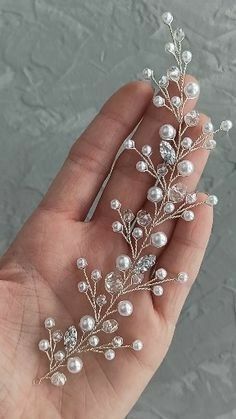 a hand holding a piece of jewelry with pearls and leaves on it's side