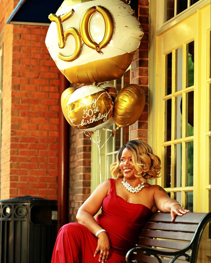 a woman in a red dress sitting on a bench next to balloons that say 50