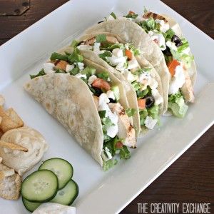 a white plate topped with three tacos next to cucumbers and crackers