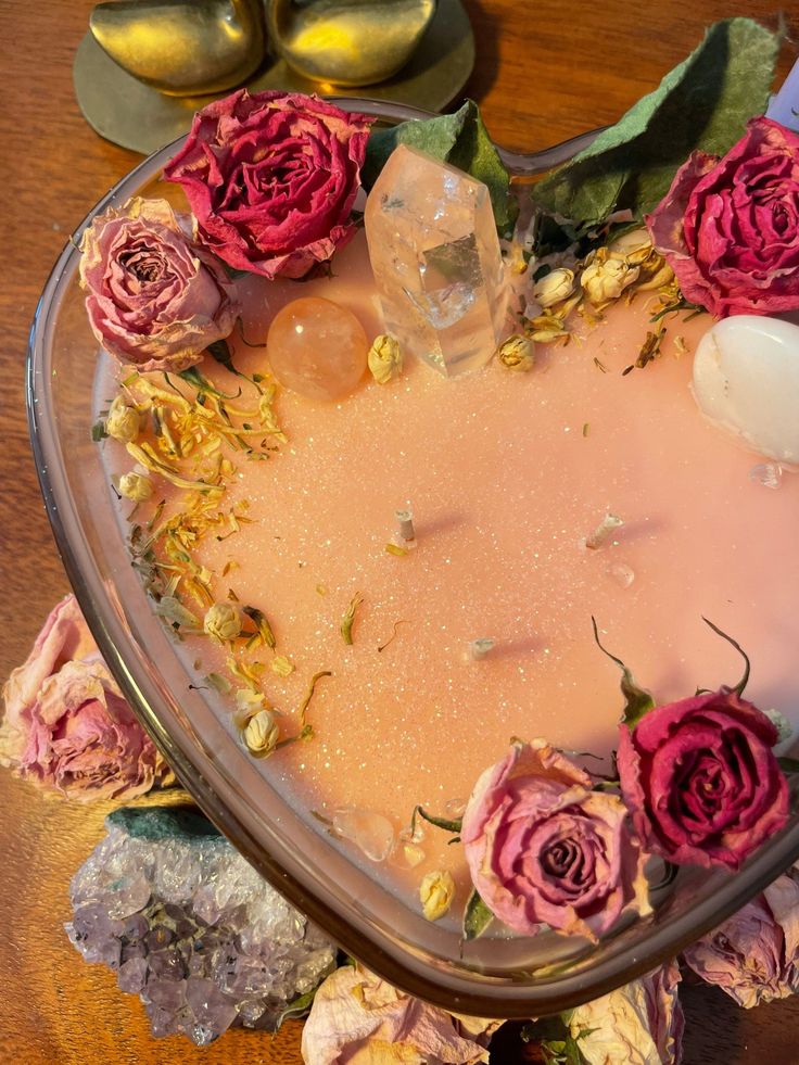 a heart shaped bowl filled with flowers on top of a wooden table