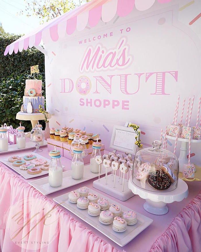 a table topped with lots of desserts next to a pink sign that says mia's donut shoppe