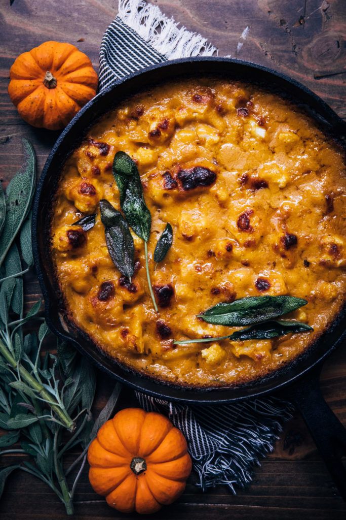 a casserole dish with pumpkins and sage on the side, surrounded by leaves