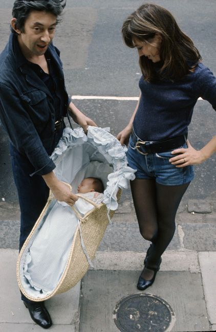 a man standing next to a woman holding a baby in a stroller on the sidewalk