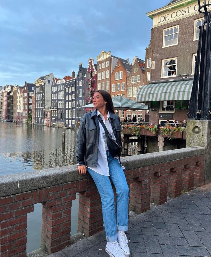 a woman is sitting on a brick wall by the water in front of some buildings